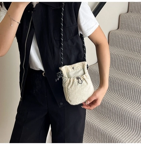 Close-up of beige drawstring mini crossbody bag with textured nylon fabric and woven strap