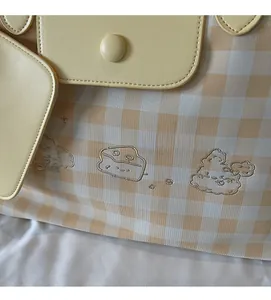 Detail of checkered shoulder bag featuring cute cartoon embroidery and yellow leather accents