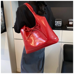 Macro shot of red glossy patent leather shoulder bag featuring a delicate bow tie detail