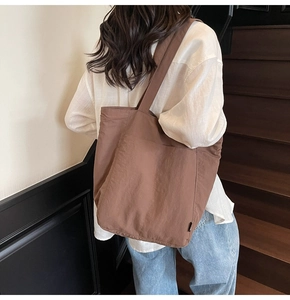 Deep brown large capacity nylon tote bag worn by a model in a minimalist indoor setting