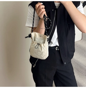 Detail of beige drawstring bucket bag with black and white woven rope shoulder strap