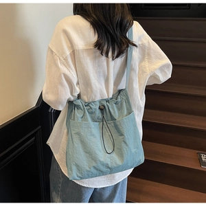 Light blue nylon bucket bag with drawstring closure and outer pocket shown on model