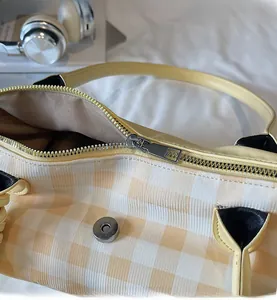 Close-up of yellow checkered tote bag featuring a smooth metal zipper and magnetic buckle
