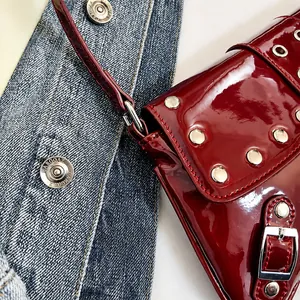 Dettaglio della borsa a spalla in vernice rosso vino con borchie argento e cuciture rosse