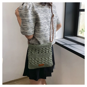 Detail of green woven crossbody bag with brown leather strap and brand patch shown on model