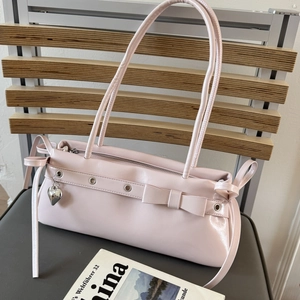 Close-up of pink shoulder bag with bow detail and silver heart pendant on wooden chair