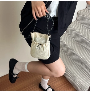 Detail of cream drawstring bucket bag with black and white woven handle and pleated texture