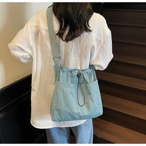 Detailed back view of a light blue nylon crossbody bag with drawstring on a female model