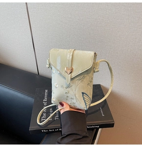 Détail d'un sac de téléphone en toile verte brodée avec fleurs et boucle coeur dorée