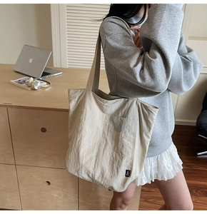 Detail of a large beige tote bag with pleated texture and black brand label