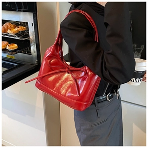 Detail of red oil wax leather shoulder bag with decorative bow and glossy finish