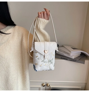 Détail du sac bandoulière blanc avec broderies florales et fermoir en cœur doré brillant