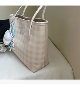 Detail of beige checkered tote bag with metal logo and soft plush pendant accessory