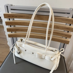 Detail of cream PU shoulder bag with bow decor, silver grommets and heart pendant