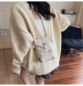 Détail de la broderie florale et fermoir en métal doré en forme de cœur sur le sac