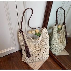 Détail du sac en paille tressée beige avec bandoulières en cuir marron et pompon décoratif