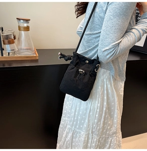 Detail of black drawstring bucket bag featuring front flap pocket and metal snap button