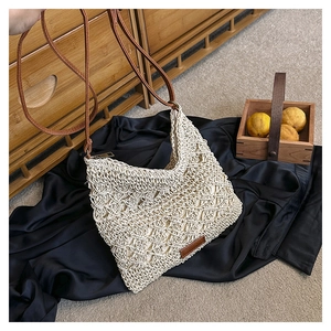 Detailed view of beige woven straw shoulder bag with brown leather strap and brand patch