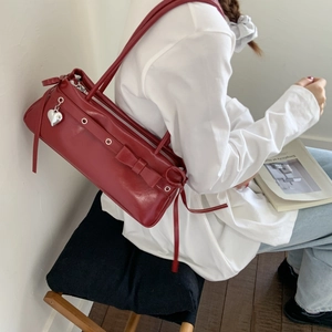 Detail view of red shoulder bag with bow, metal eyelets and a heart pendant