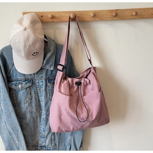 Detail view of pink nylon drawstring shoulder bag with adjustable strap and front pocket