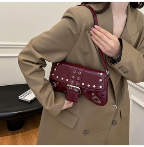 Detalle de bolso bajo el brazo de cuero de charol burdeos con tachuelas en una modelo