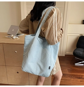 Close-up of light blue pleated nylon tote bag on a wooden desk with office essentials