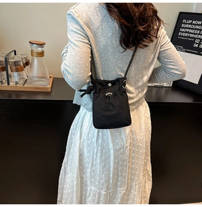Rear view of a black nylon drawstring crossbody bag worn by a model in a modern room