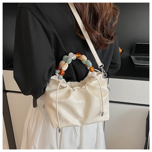 Detail of cream pleated bucket bag with colorful translucent beaded handle on a model
