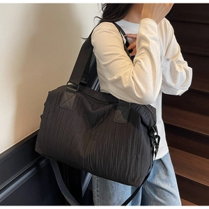 Detail of black large capacity travel bag with pleated texture and wide woven shoulder straps