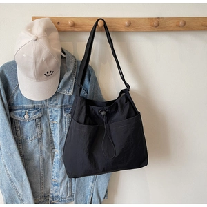 Detail of black nylon tote bag with drawstring closure and front pockets on a wooden hook