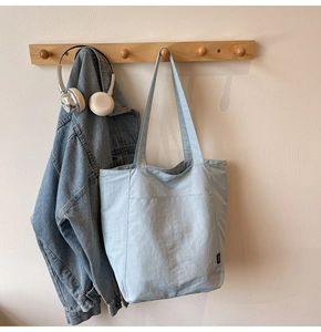Close-up of a light blue canvas tote bag with outer pocket hanging on a wooden hook