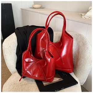 Macro shot of two red glossy PU leather tote bags with elegant bow details on a white chair
