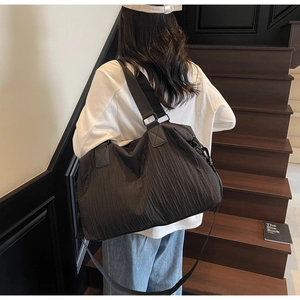 Detail view of a large black pleated canvas tote bag worn by a model on stairs
