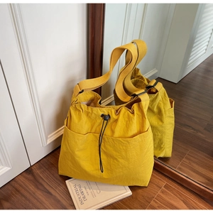 Detail of a large yellow nylon bucket bag with drawstring and wide woven strap