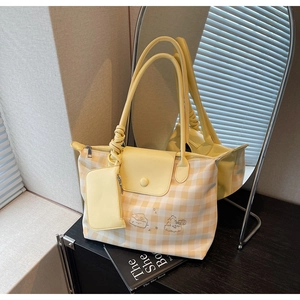 Detail view of yellow checkered tote bag with cartoon embroidery and small hanging pouch