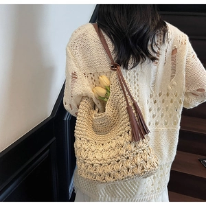 Détail de la texture d'un sac en paille avec bandoulière en cuir brun et pompon