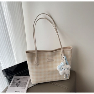 Detail view of beige checkerboard tote bag with plush star charm and logo plaque