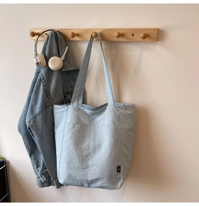 Detail view of large capacity tote bag with exterior pocket hanging on a wooden hook