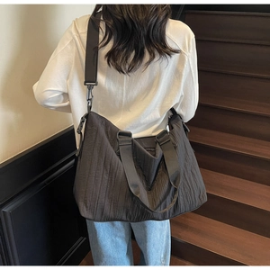 Detail of black pleated canvas tote showing textured fabric and wide shoulder strap