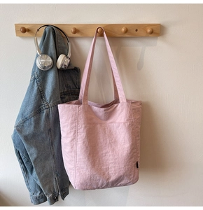 Minimalist pink tote bag hanging on wooden hooks with a casual denim jacket and headphones