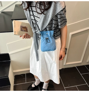 Close-up of light blue drawstring bucket bag with black strap worn with a striped top