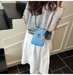 Detail of light blue nylon crossbody bucket bag with drawstring and bicolour strap