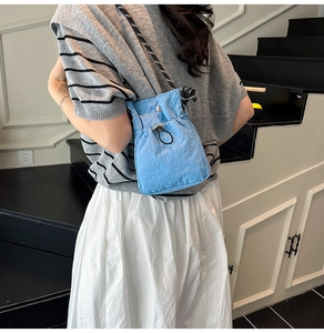 Detail of blue drawstring bucket bag with black and white woven rope shoulder strap