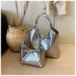 Detail view of large and small silver metallic tote bags with bow knot accents on a rug