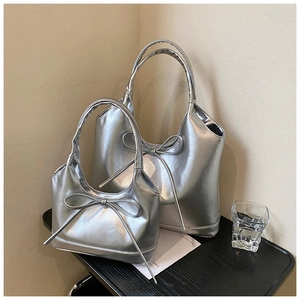 Detail of silver bow-knot PU leather tote bags in large and small sizes on a black tray