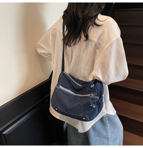 Detail view of deep blue denim crossbody bag with multiple zippers and rivets