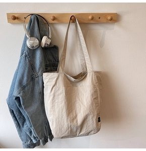 Detail of light beige tote bag hanging with denim jacket and headphones in a lifestyle setting