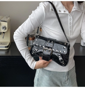 Close-up of black patent leather underarm bag with silver rivets and buckles