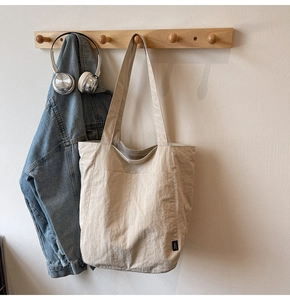 Detail of minimalist beige tote bag hanging with denim jacket on wooden hook