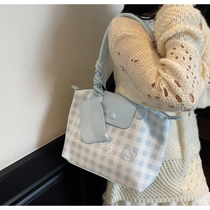 Detail of blue plaid tote bag featuring twisted rope handle and cartoon character charm